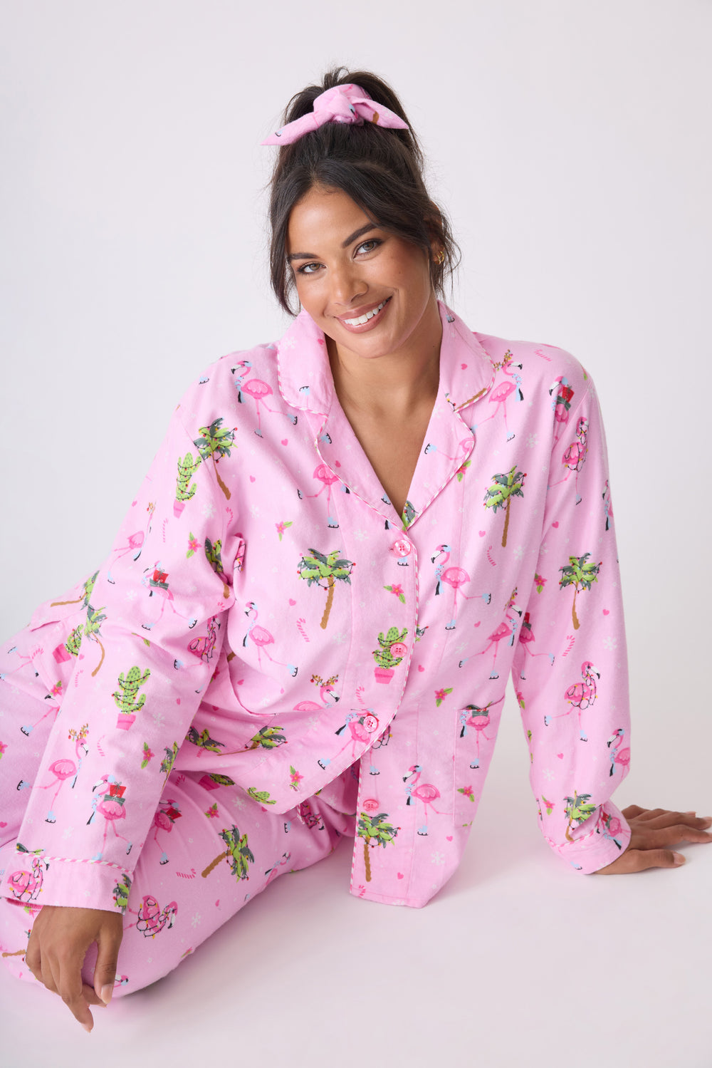 Women's cotton flannel pajama set in pink with retro flamingo print. Button-front collared top & tie-waist pant. Embroidered sleeve cuff "Let's Jingle & Flamingle". Includes matching hair wrap.