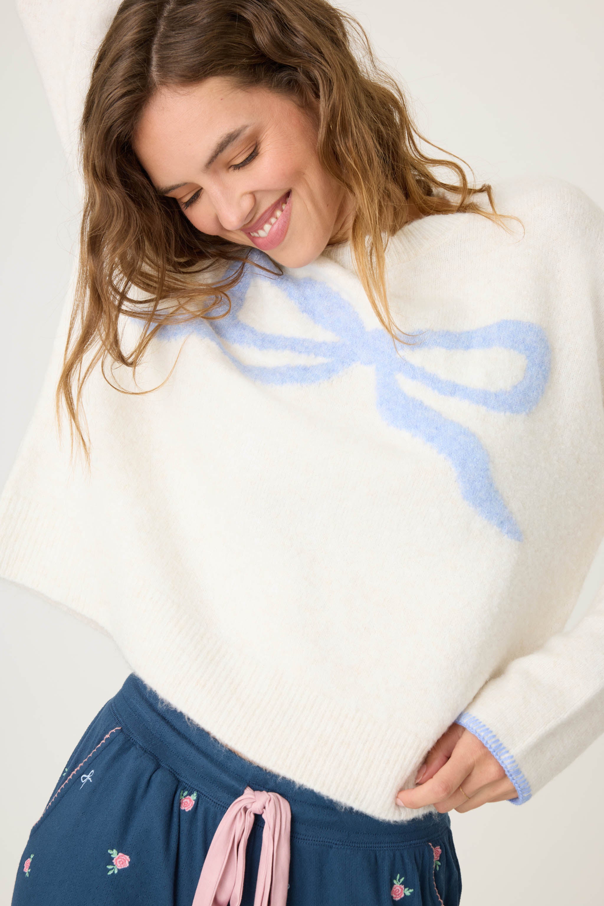 Women's ivory snuggle sweater with pink bow knitted graphic on front.